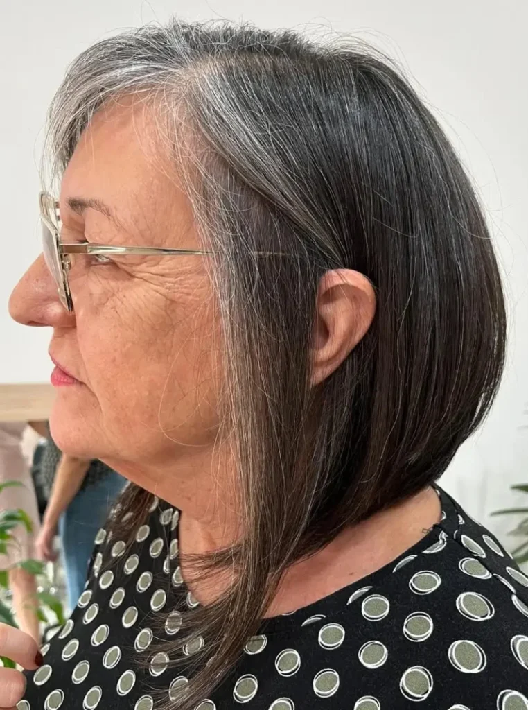 Frau über 60 mit asymmetrischem Bob, längere Vorderpartie und dunkles Haar mit grauen Strähnen für einen modernen und stilvollen Look.