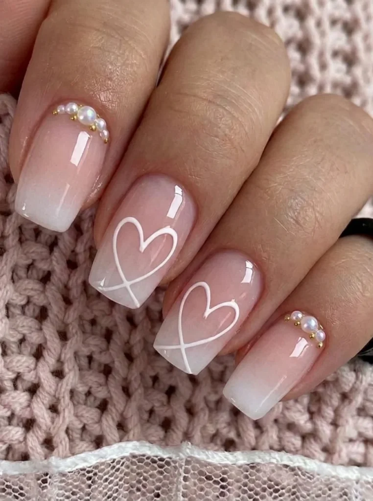 Kurze Babyboomer French Nägel mit weißem Ombre-Effekt, feiner Herz Nail Art und kleinen Perlen auf eleganten rosa Nude-Nägeln.