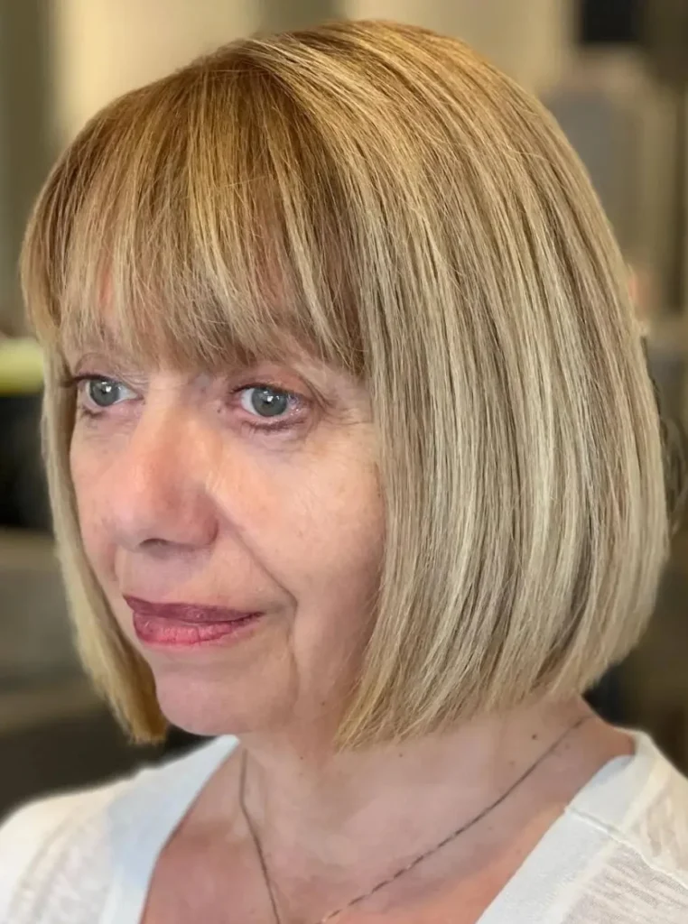 Frau über 60 mit Blunt Bob und geradem Pony, glatter blonder Bob mit klaren Linien für einen eleganten und modernen Look.