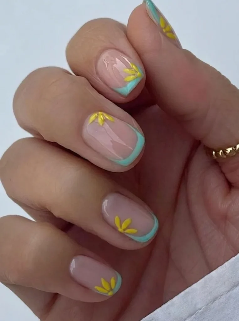 Kurze bunte French Nägel mit hellblauen Spitzen und kleinen gelben Blumen auf einer glänzenden Nude-Basis für einen frischen Frühlingslook.