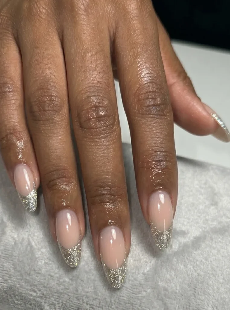 Glitzer weiße French Nails mit funkelnden silbernen Spitzen und glänzendem Nude-Finish auf mandelförmigen Nägeln.