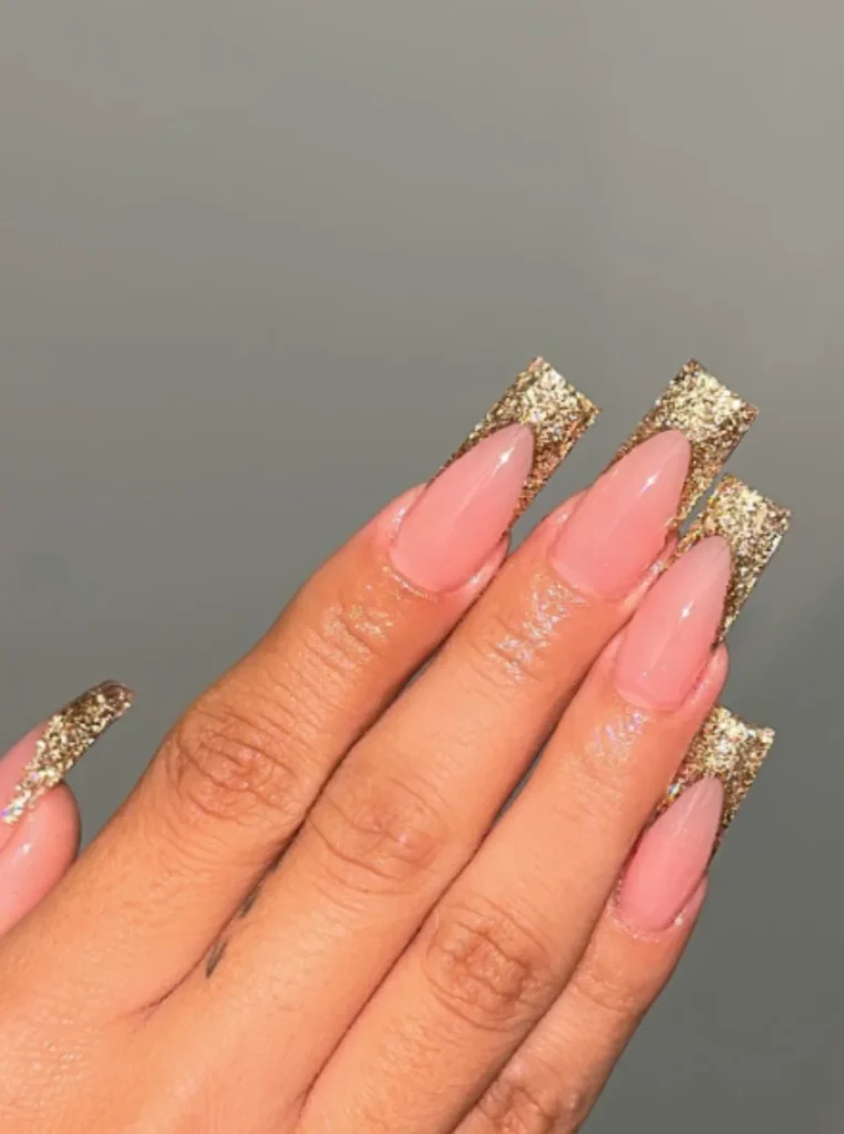 Elegante Gold-Glitzer French Nägel mit glänzender Nude-Basis auf langen Coffin-Nägeln in glamouröser Nahaufnahme.