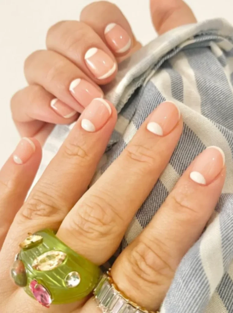 Minimalistische weiße French Nails mit kleinen weißen Punkten und glänzendem Nude-Finish auf kurzen natürlichen Nägeln.