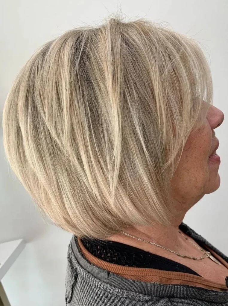 Frau über 60 mit kurzem gestuftem Bob und blonden Highlights, voluminöse Frisur mit weichen Stufen für einen modernen und jugendlichen Look.