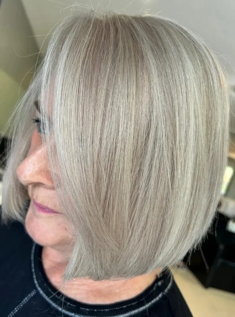 Frau über 60 mit langem Bob in Silberblond, glatte schulterlange Haare mit Seitenscheitel für einen eleganten und jugendlichen Look.