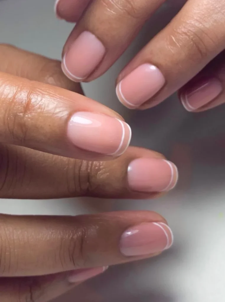 Minimalistische weiße French Nägel mit feinen weißen Linien und glänzendem Nude-Finish auf kurzen natürlichen Nägeln.