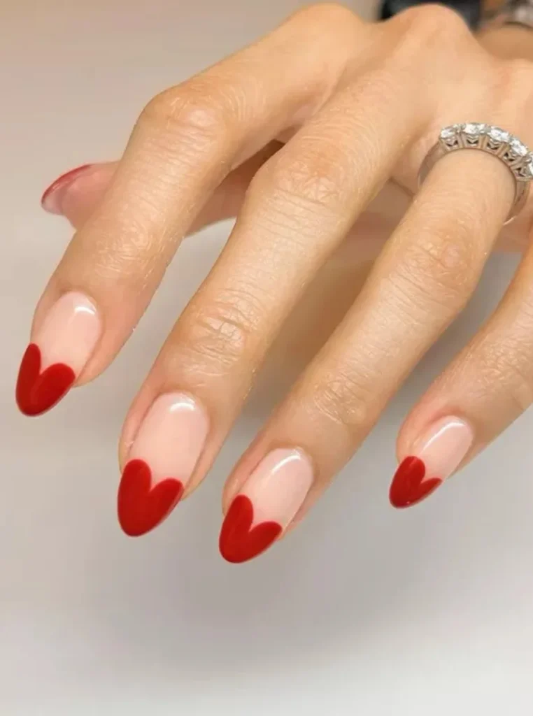 Moderne Nägel French Farbe mit roten Herzspitzen auf eleganten mandelförmigen Nude Nägeln