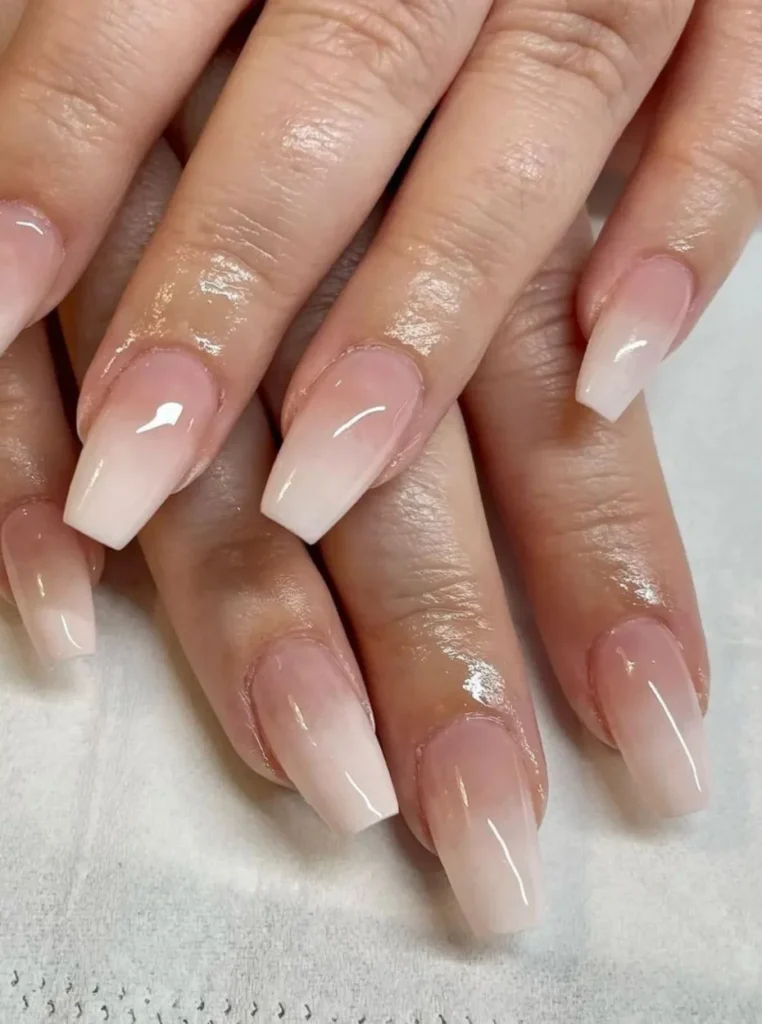 Elegante Ombre French Nägel im Baby-Boomer-Stil mit sanftem Rosa-Weiß-Verlauf auf glänzenden Coffin-Nägeln in Nahaufnahme.