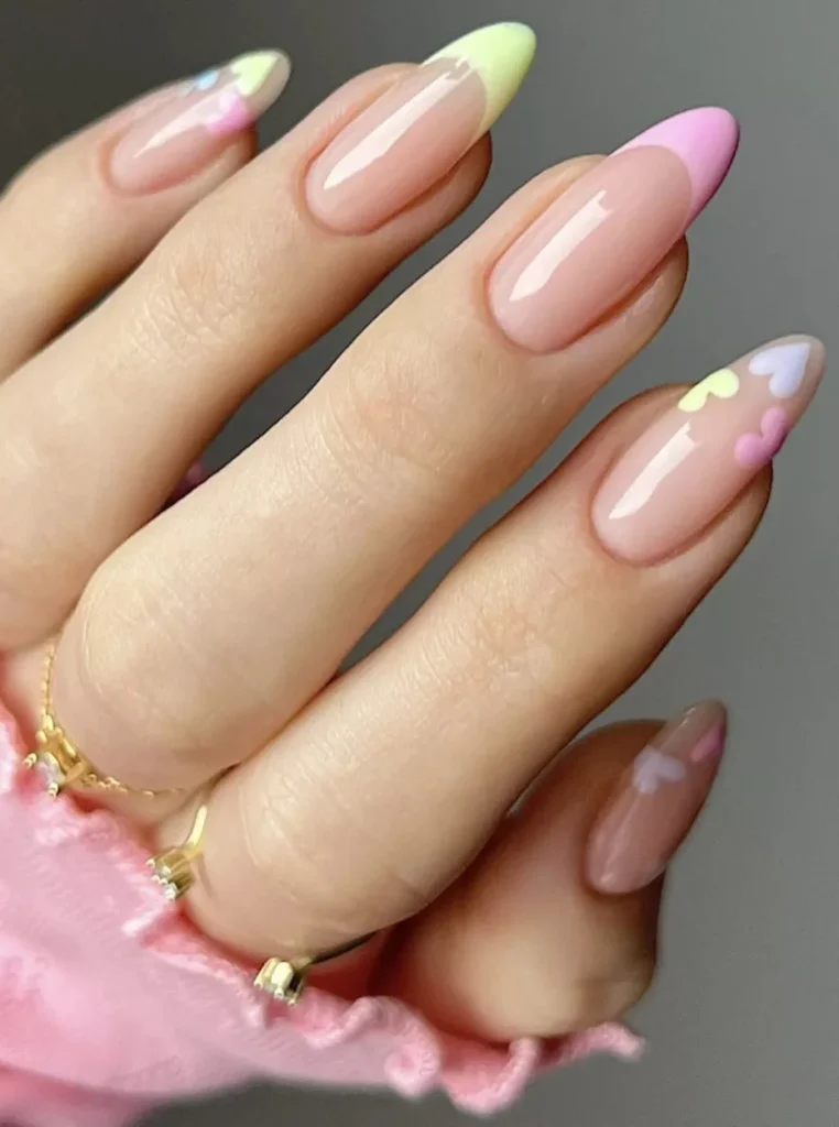 Verspielte Pastell French Nägel mit rosa und grünen Spitzen sowie kleinen Herzdetails auf mandelförmigen Nägeln in süßer Nahaufnahme.
