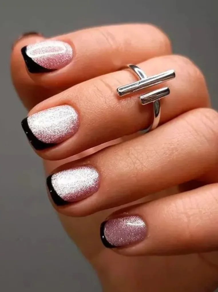 Moderne kurze French Nägel mit schwarzen Spitzen und schimmernder rosa Silber-Basis auf eleganten gepflegten Händen.