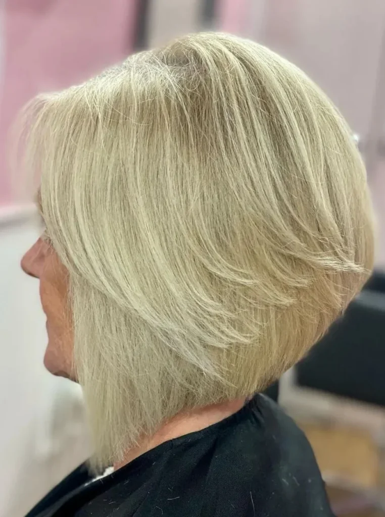 Frau über 60 mit umgekehrtem Bob, hellblondem Haar und gestuftem Hinterkopf für mehr Volumen und einen modernen, eleganten Look.