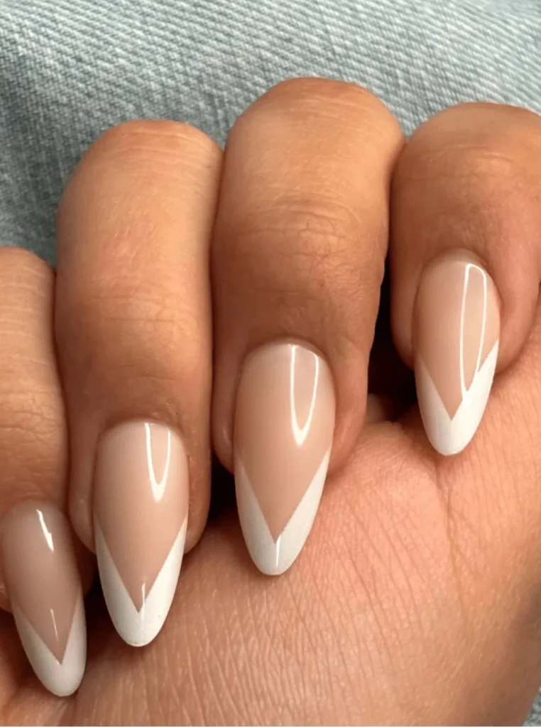 V-Shape weiße French Nägel mit elegantem Nude-Finish und spitzen weißen French-Spitzen auf mandelförmigen Nägeln.