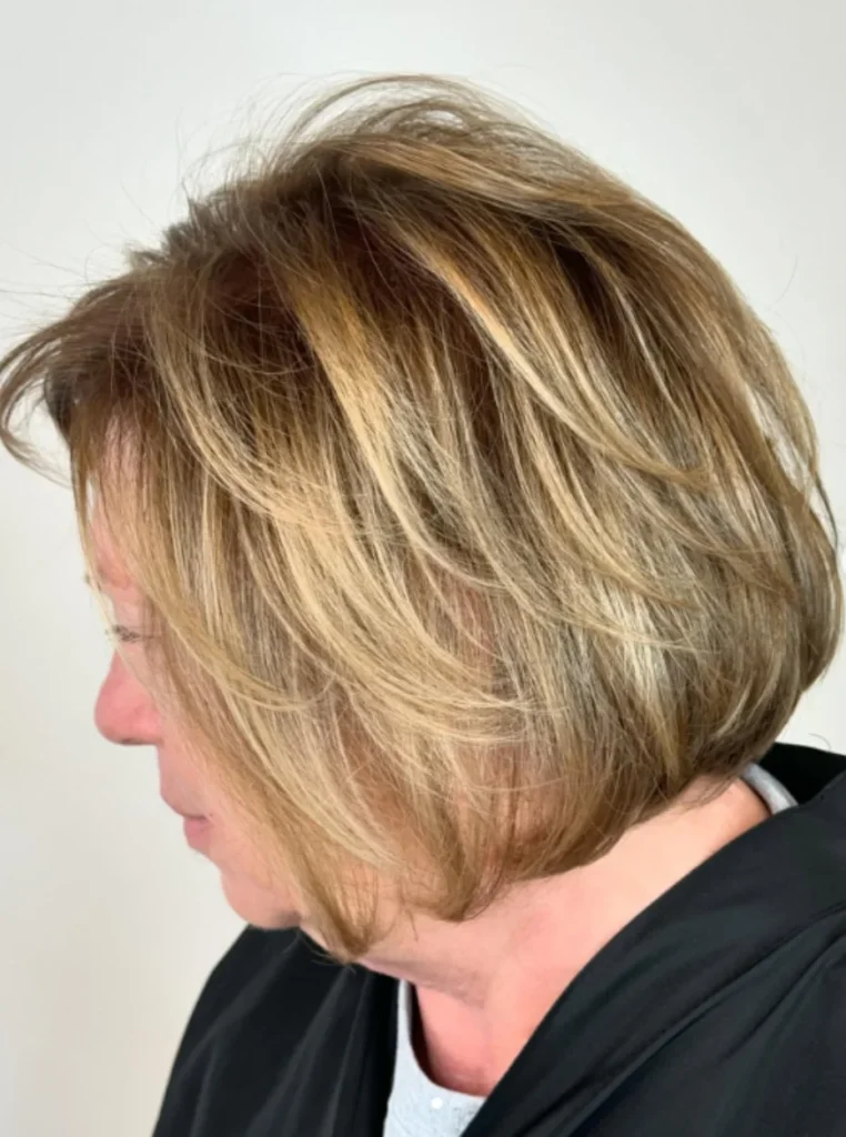 Frau über 60 mit weichem Bob und Federstufen, blondes Haar mit sanften Highlights für mehr Bewegung, Volumen und einen jugendlichen Look.