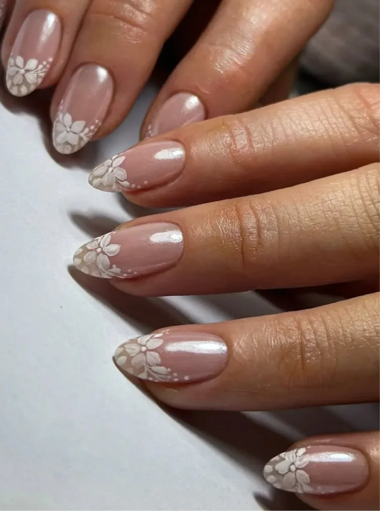 Weiße French Nägel mit zartem Blumen-Design und glänzendem Perl-Finish auf eleganten mandelförmigen Nägeln.