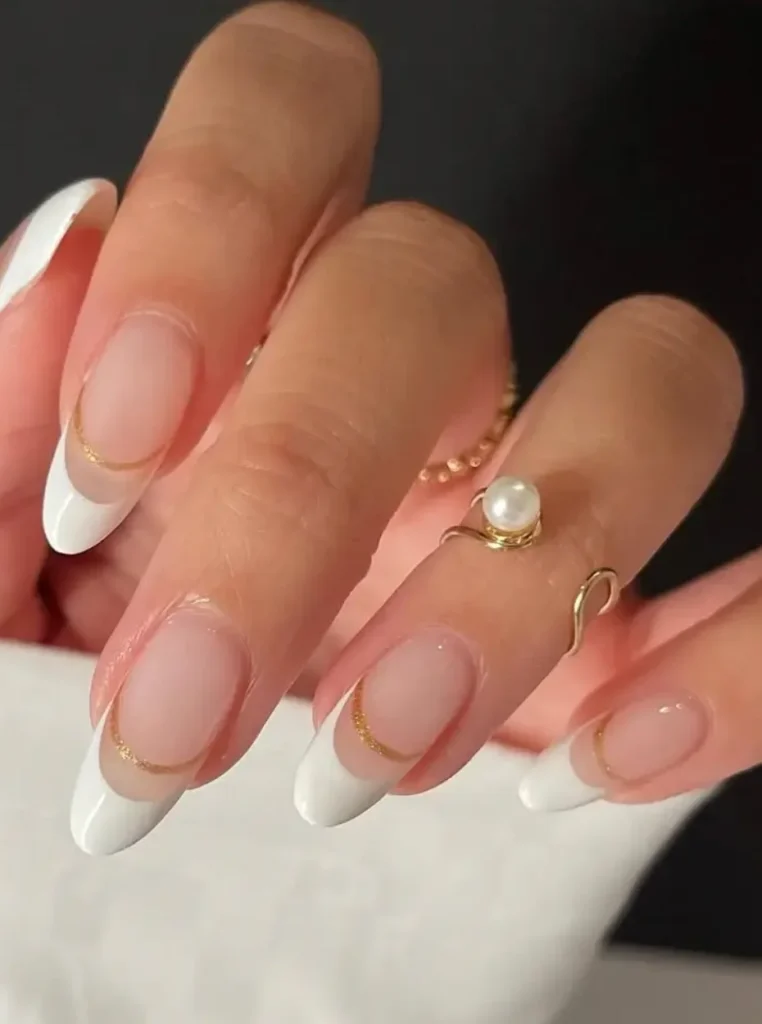 Weiße French Nägel mit goldenen Details und glänzendem Nude-Finish auf eleganten mandelförmigen Nägeln.