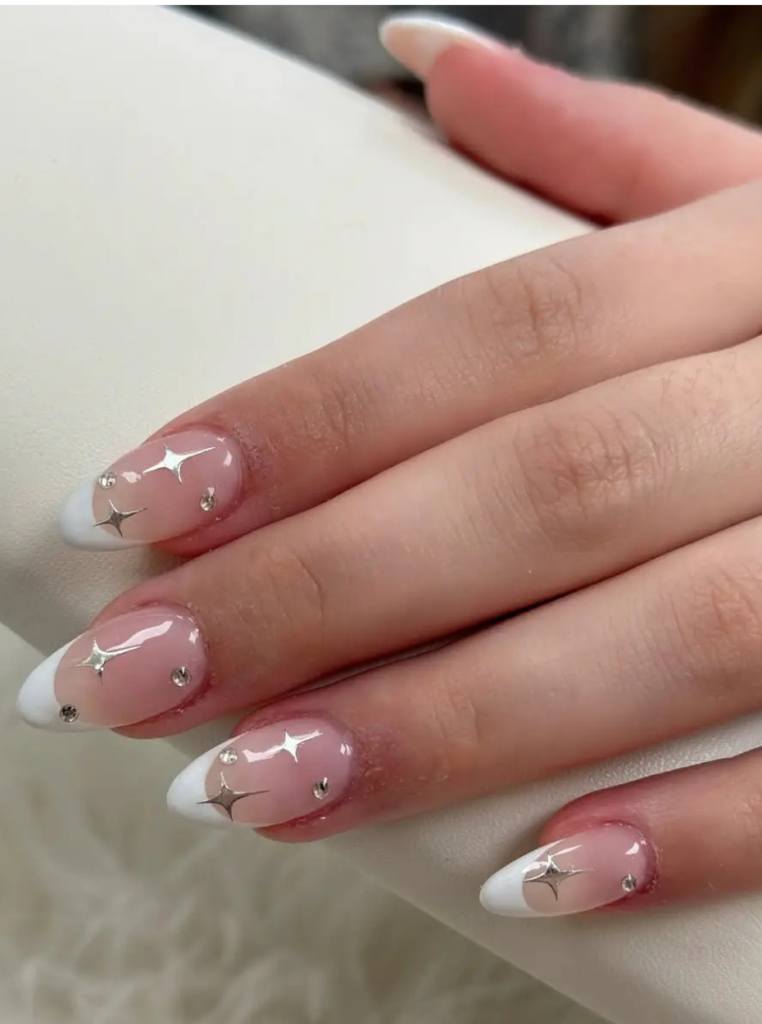 French Nails mit Strasssteinen, silbernem Stern-Design und glänzendem Nude-Finish auf eleganten mandelförmigen Nägeln.