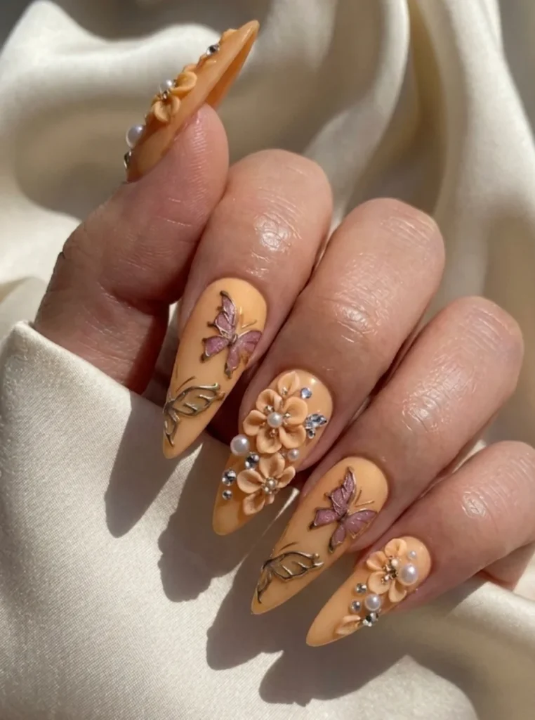 Apricot 3D Blumen Nägel mit Perlen, Schmetterlingen und Strasssteinen auf langen spitzen Nägeln.