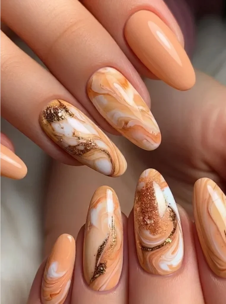 Apricot Marmor Nägel mit weißen Wirbelmustern und goldenen Akzenten auf mandelförmigen Nägeln.