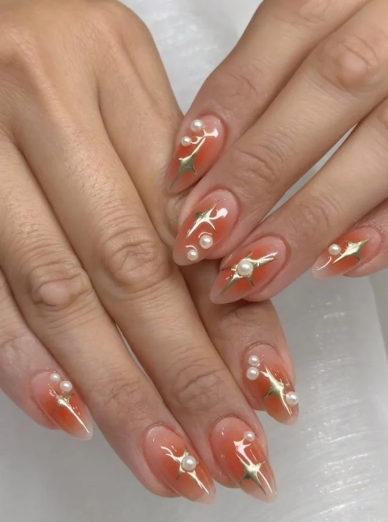 Apricot Pearl Nägel mit Perlenverzierungen und goldenen Akzenten auf mandelförmigen Nägeln.