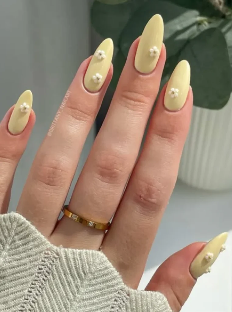 Butter Yellow Almond Nails mit kleinen weißen Blumen-Akzenten auf mandelförmigen Nägeln – elegantes Frühlingsdesign