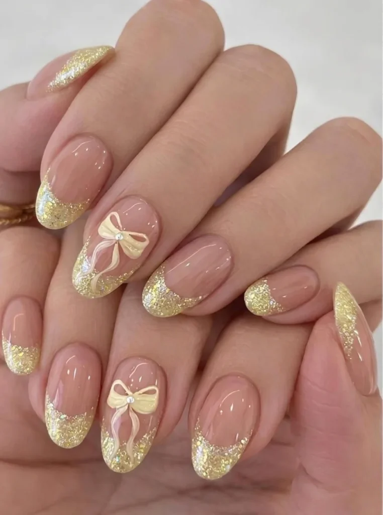 Butter Yellow Nagel mit goldenen Glitzer-French-Spitzen und 3D-Schleifen auf ovalen Nägeln