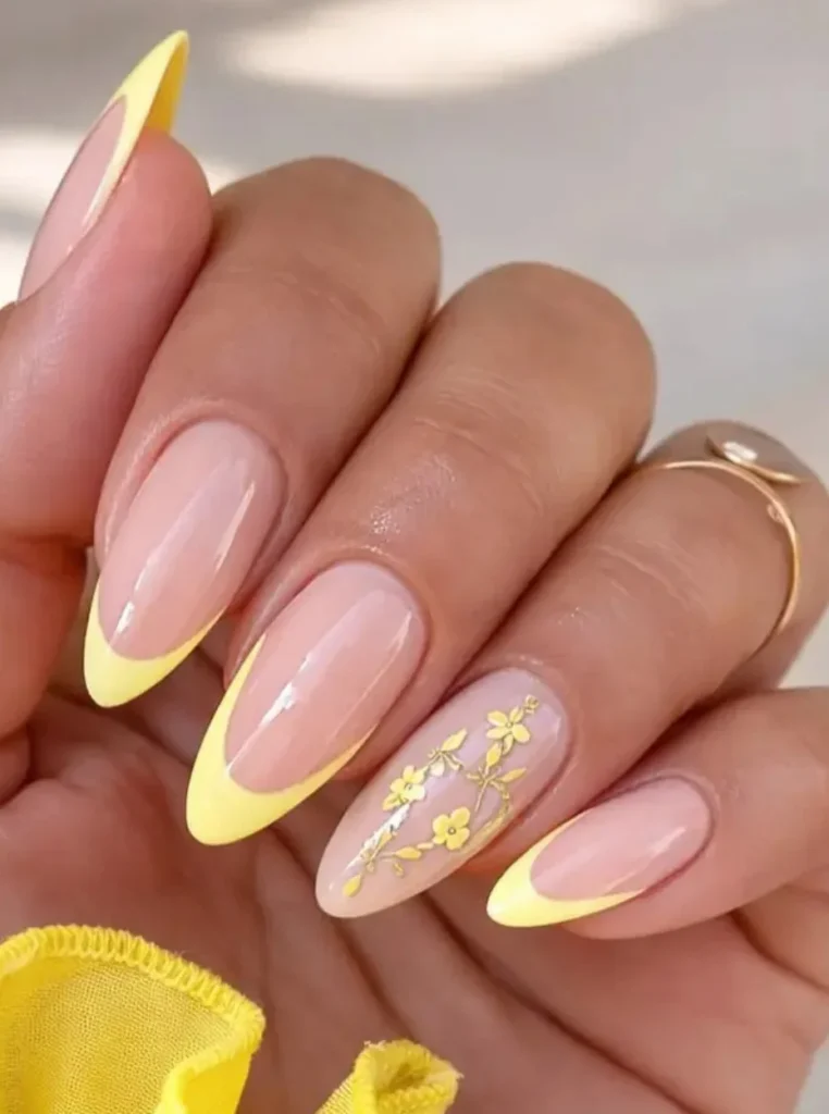 Buttergelbe French Nägel mit zarten Blumenakzenten, glänzender Nude-Basis und eleganten mandelförmigen Nägeln.