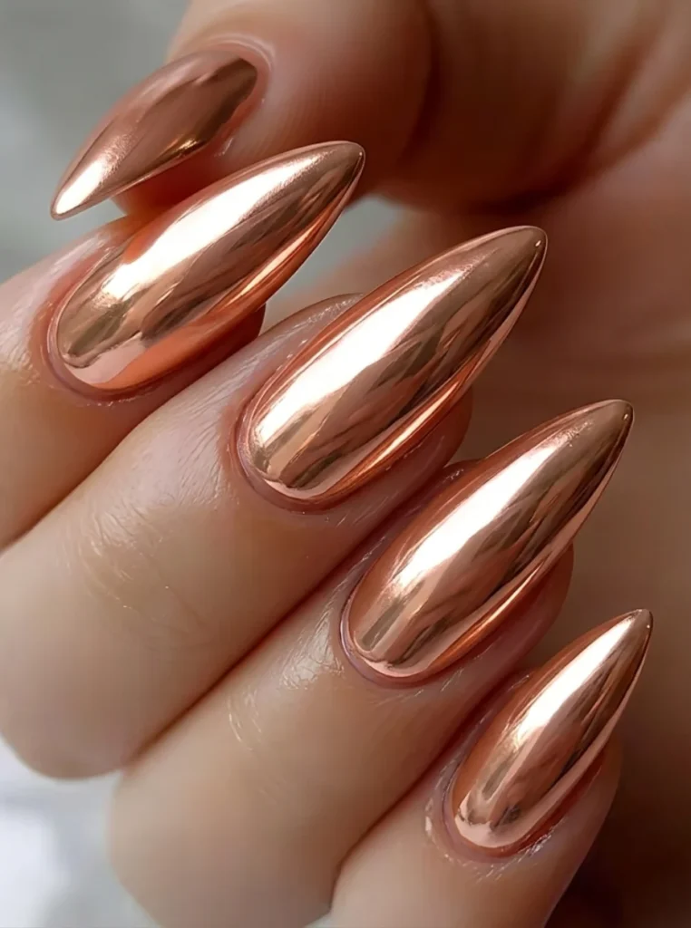 Chrome Pfirsich Nägel mit spiegelndem Roségold-Effekt auf langen mandelförmigen Nägeln.