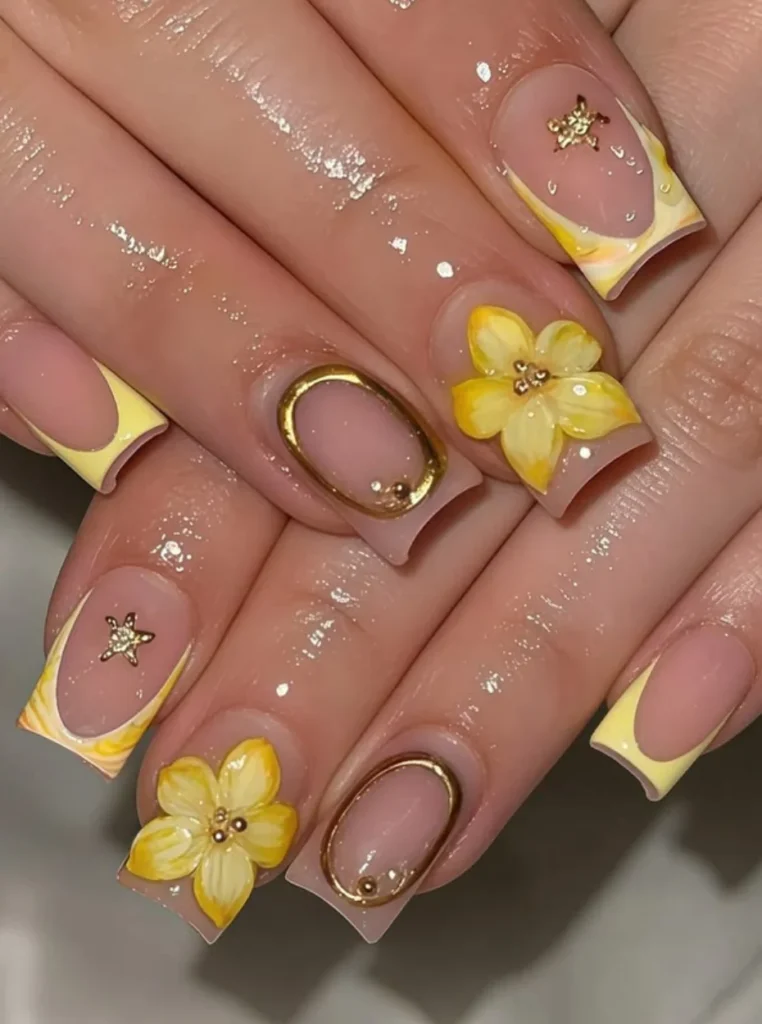 Gelb French Nägel mit 3D-Blumen, goldenen Akzenten und glänzender Nude-Basis auf eckigen Nägeln.