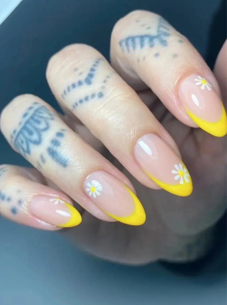 Gelb French Nägel mit kleinen Gänseblümchen, leuchtend gelben Spitzen und glänzender Nude-Basis auf mandelförmigen Nägeln.