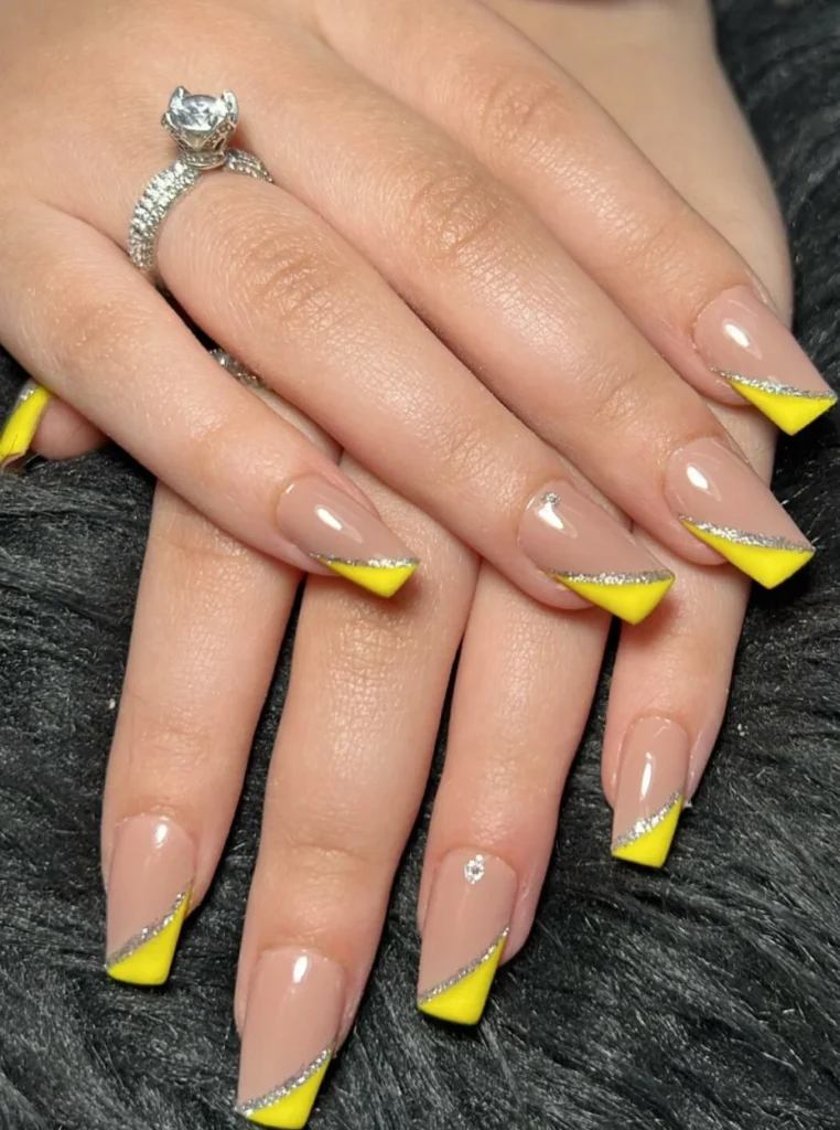 Gelb French Nägel mit silberner Glitzerlinie, nude Basis und modernem schrägem French-Design auf eckigen Nägeln.