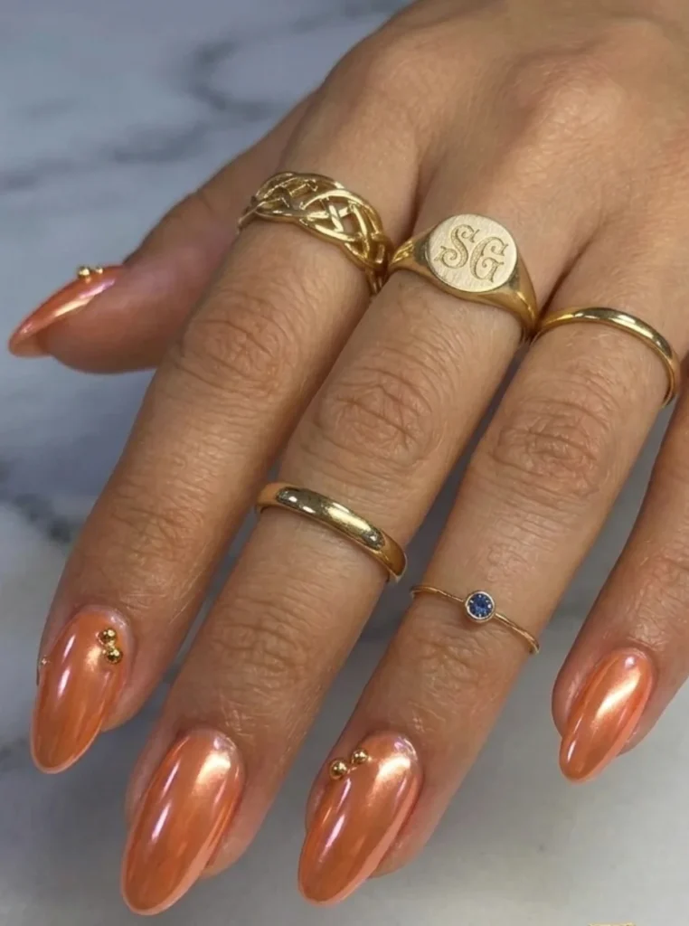 Glazed Apricot Nägel mit schimmerndem Perlglanz-Effekt auf mandelförmigen Nägeln und eleganten Goldakzenten.