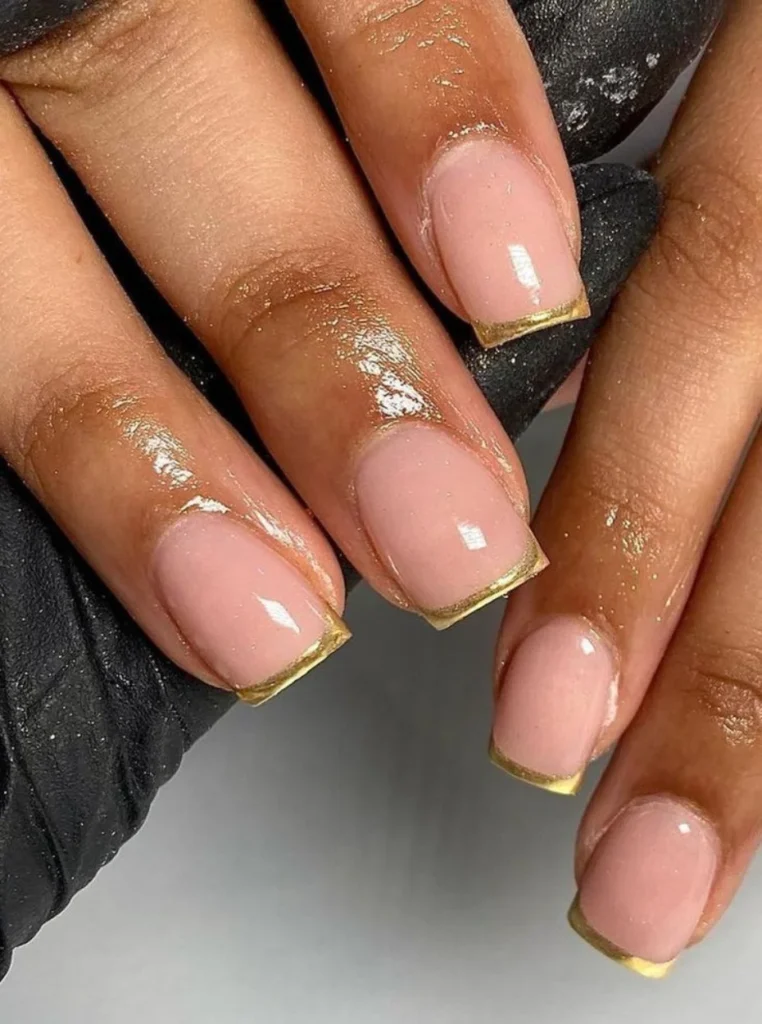 Elegante kurze French Nägel mit glänzender Nude-Rosa Basis und feinen goldenen Spitzen für einen luxuriösen und zeitlosen Nagellook.