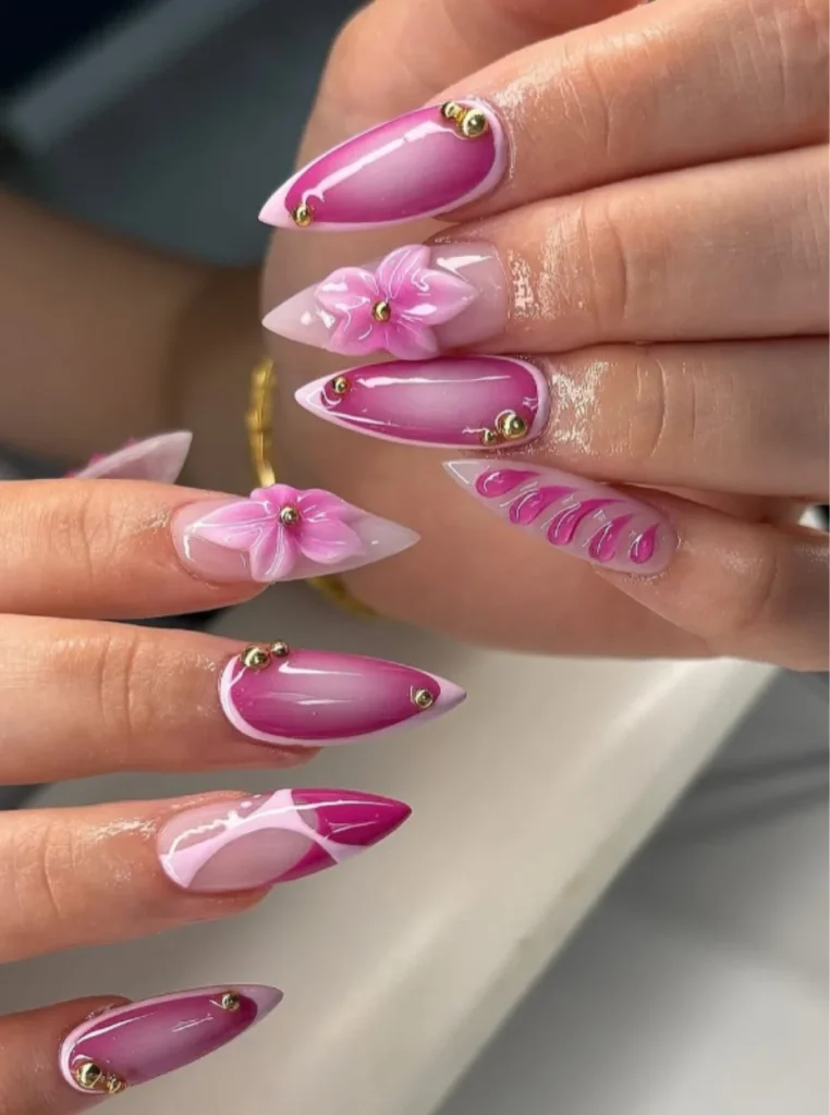 3D-Blumen Nägel in Pink mit handmodellierten Blüten, glänzendem Ombre-Effekt und goldenen Akzenten auf spitzen Nägeln – auffälliger Nageltrend Frühling 2026.