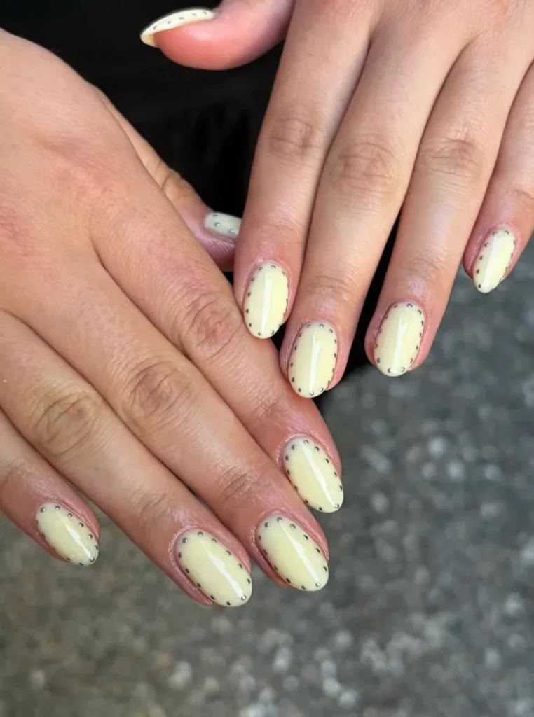 Buttergelbe Nägel mit glänzendem Finish und feinen Punktdetails auf kurzen ovalen Nägeln – trendiges Frühlings-Nageldesign 2026.