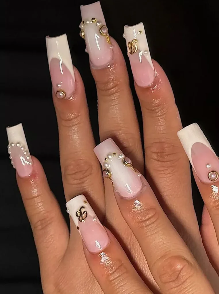 Nude Nägel mit Perlen, weißen French-Spitzen und goldenen Schmuckdetails auf langen eckigen Nägeln – luxuriöses Nageldesign für den Frühling 2026.