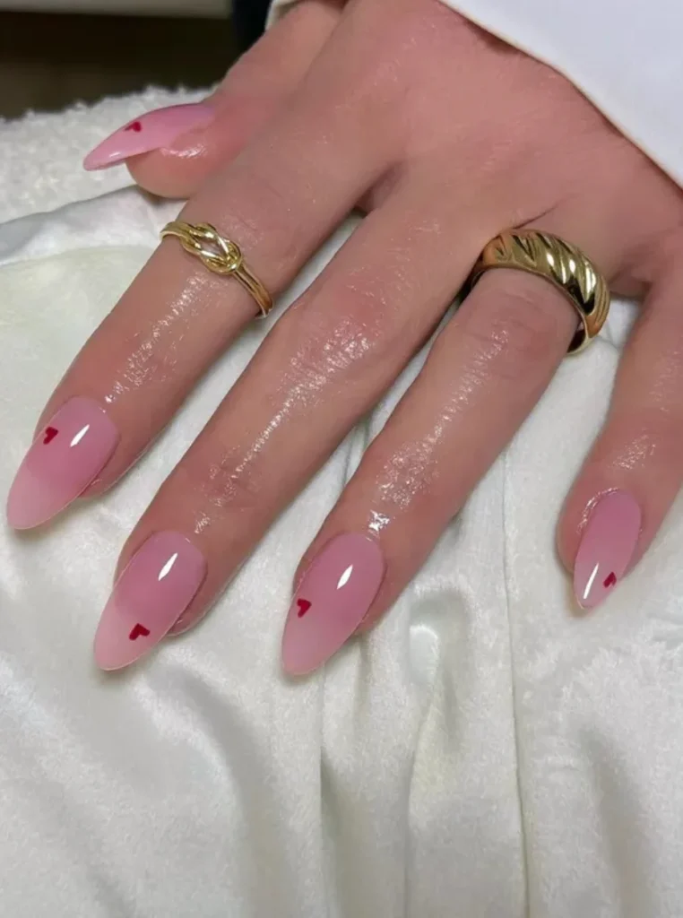 Strawberry Milk Nägel in zartem Babyrosa mit kleinen roten Herzchen auf mandelförmigen Nägeln – süßer Nageltrend für den Frühling 2026.