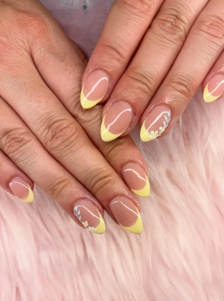 Pastellgelbe French Nails mit zarten weißen Blumenmustern auf mandelförmigen Nägeln und natürlicher Nude-Basis.