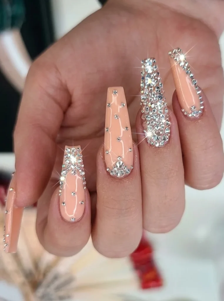 Pfirsich Nägel mit funkelnden Strasssteinen, Kristallverzierung und glamourösem Nail-Art-Design auf langen eckigen Nägeln.