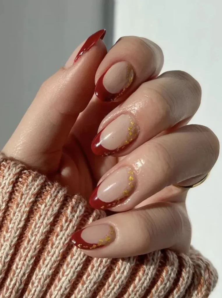 Elegante rote French Nägel mit tiefroten Spitzen, goldenen Akzenten und glänzender Nude-Basis für einen stilvollen und modernen Nagellook.