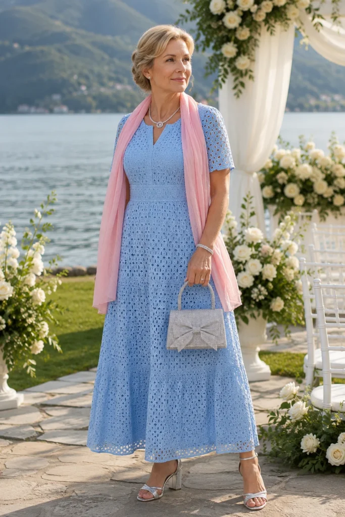 Elegantes Brautmutter Outfit Sommer mit hellblauem Spitzenkleid, rosa Schal, silberner Handtasche und Sandaletten bei einer romantischen Hochzeit am See.